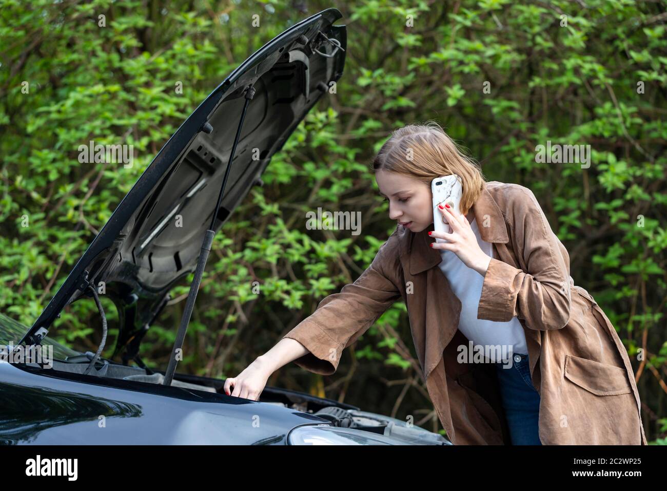 Una donna impotente che ha chiesto aiuto/assistenza per cercare un'auto rotta, si è fermata sul lato della strada. Non capisce cosa è successo. Foto Stock