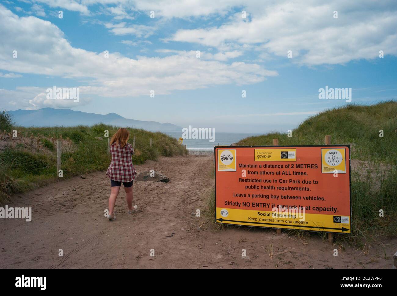 County Kerry, Irlanda - 14 giugno 2020: Donna che cammina verso la spiaggia sulla costa occidentale della contea di Kerry, Covid-19 segno di allontanamento sociale all'entrata Foto Stock