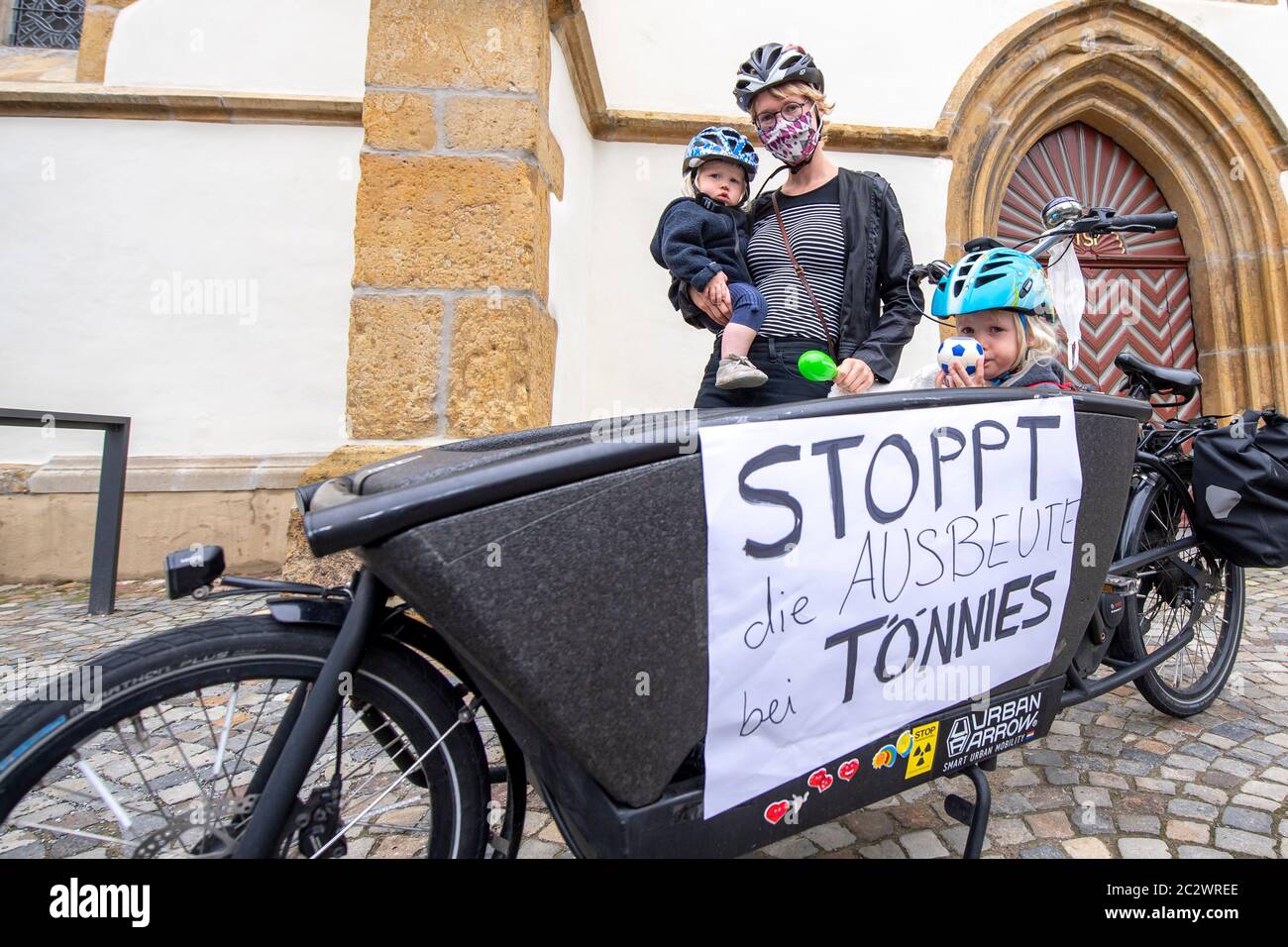 18 giugno 2020, Renania Settentrionale-Vestfalia, Rheda-Wiedenbrück: Nicole Ritschel è venuto con le sue figlie Paula (l.) e Frieda su una bicicletta alla veglia per la situazione nella fabbrica di carne di Tönnies sulla piazza del mercato di Rheda-Wiedenbrück. Sulla bicicletta è presente un cartello con l'iscrizione 'Stoppt die Ausbeute bei Tönnies'. Il virus è stato rilevato in più di 600 dipendenti della Tönnies Meat Company. L'impianto di Tönnies verrà chiuso il più possibile. Foto: David Inderlied/dpa Foto Stock