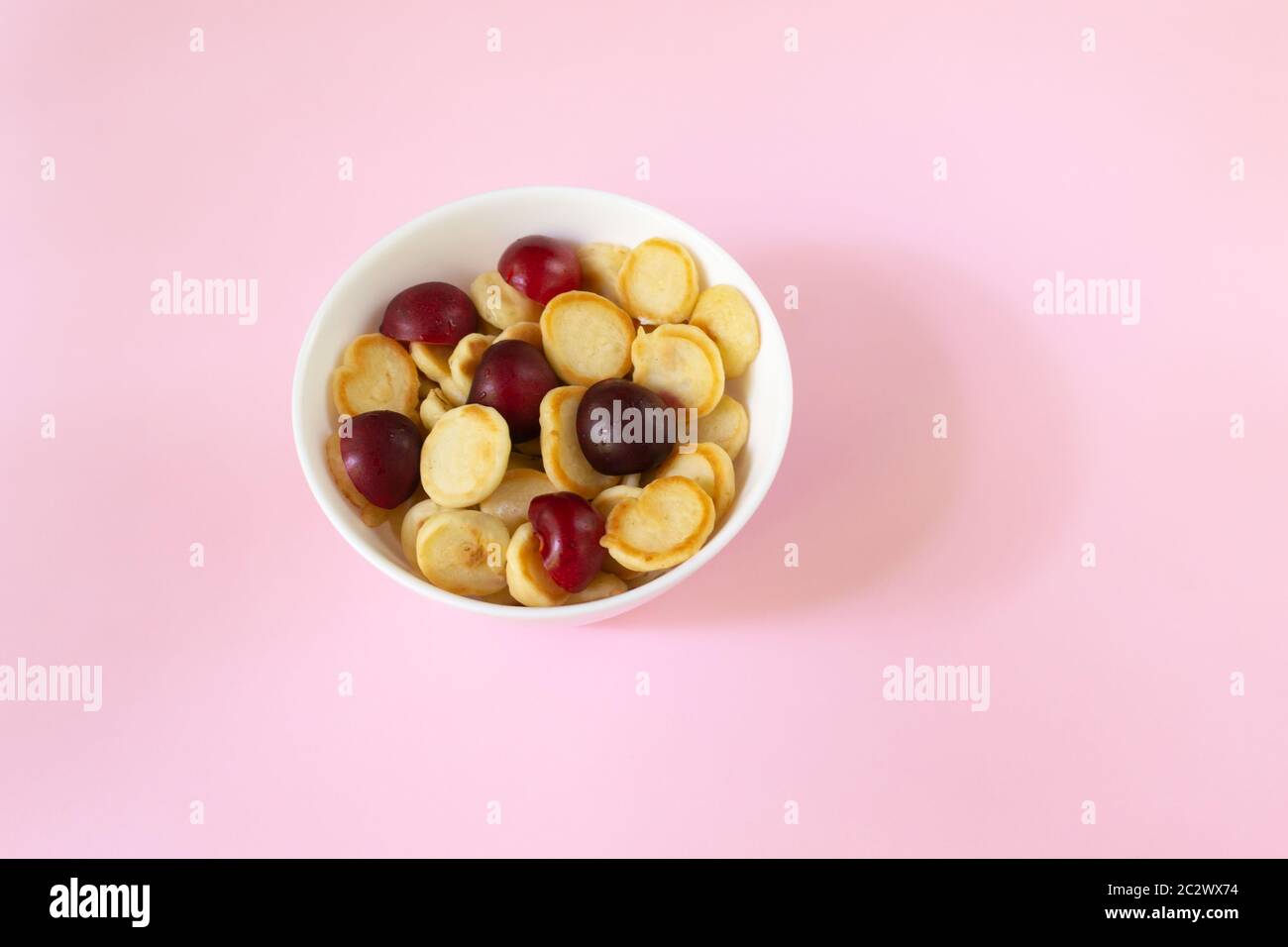 Ciotola bianca con minuscola frittella di cereali con ciliegia dolce su sfondo rosa. Spazio di copia. Cucina alla moda. Foto Stock
