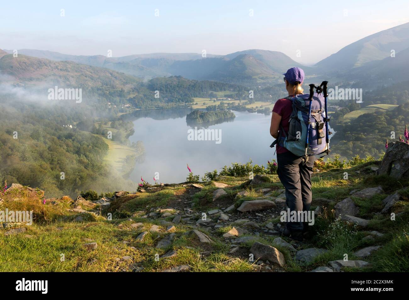 Walker godendo della vista sul lago Grasmere da Loughrigg cadde in una mattinata estiva misty, Lake District, Cumbria, UK Foto Stock