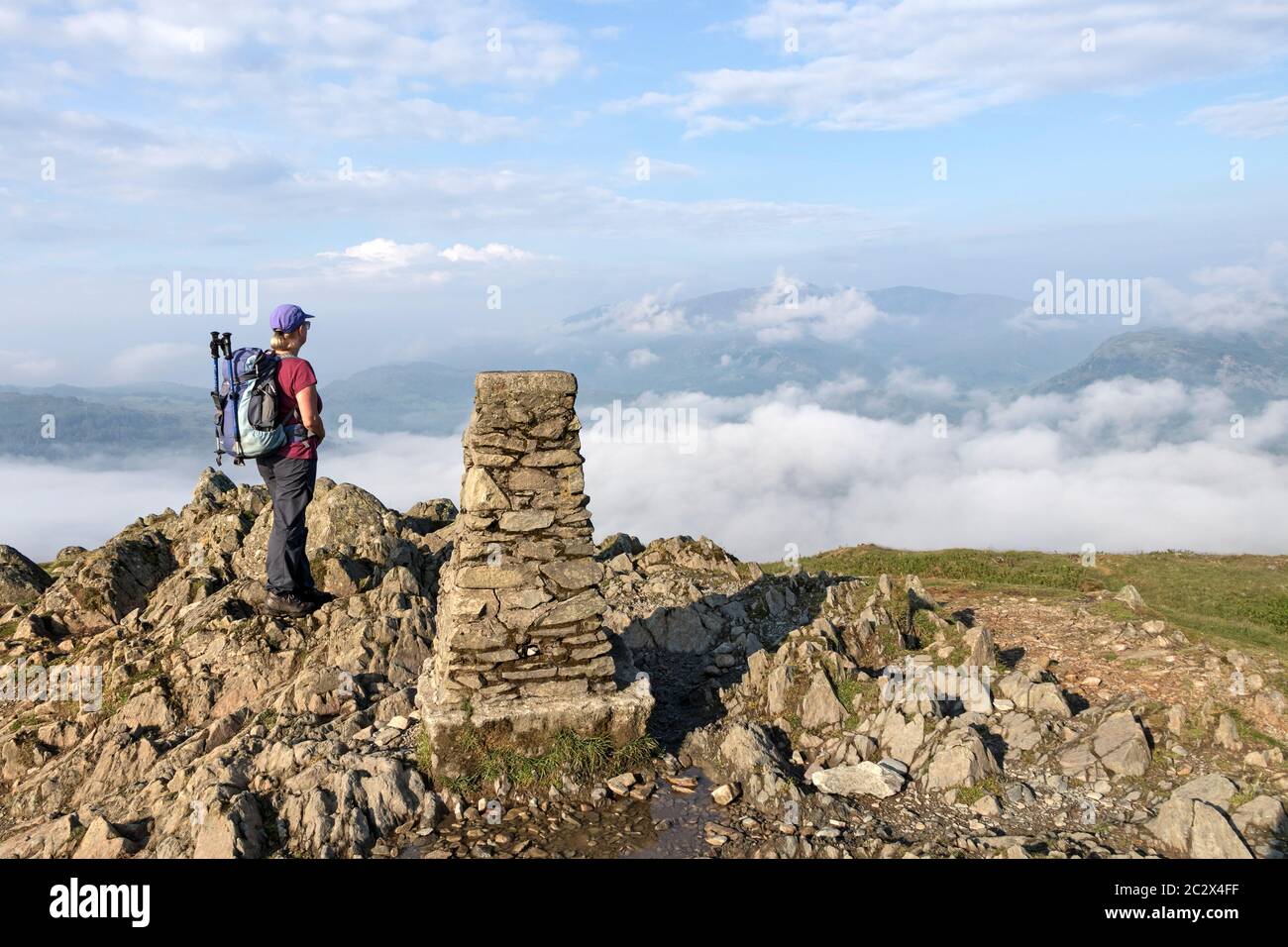 Walker godendo della vista ovest dalla cima di Loughrigg cadde sopra le valli riempite di nuvole, Lake District, Cumbria, Regno Unito Foto Stock