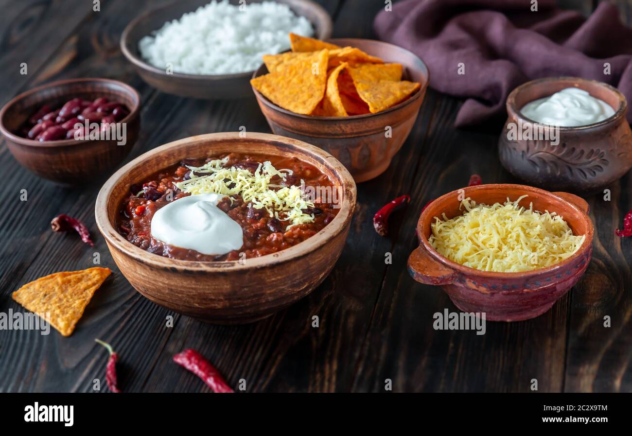 Ciotola di chili con carne con condimenti su un tavolo di legno Foto Stock