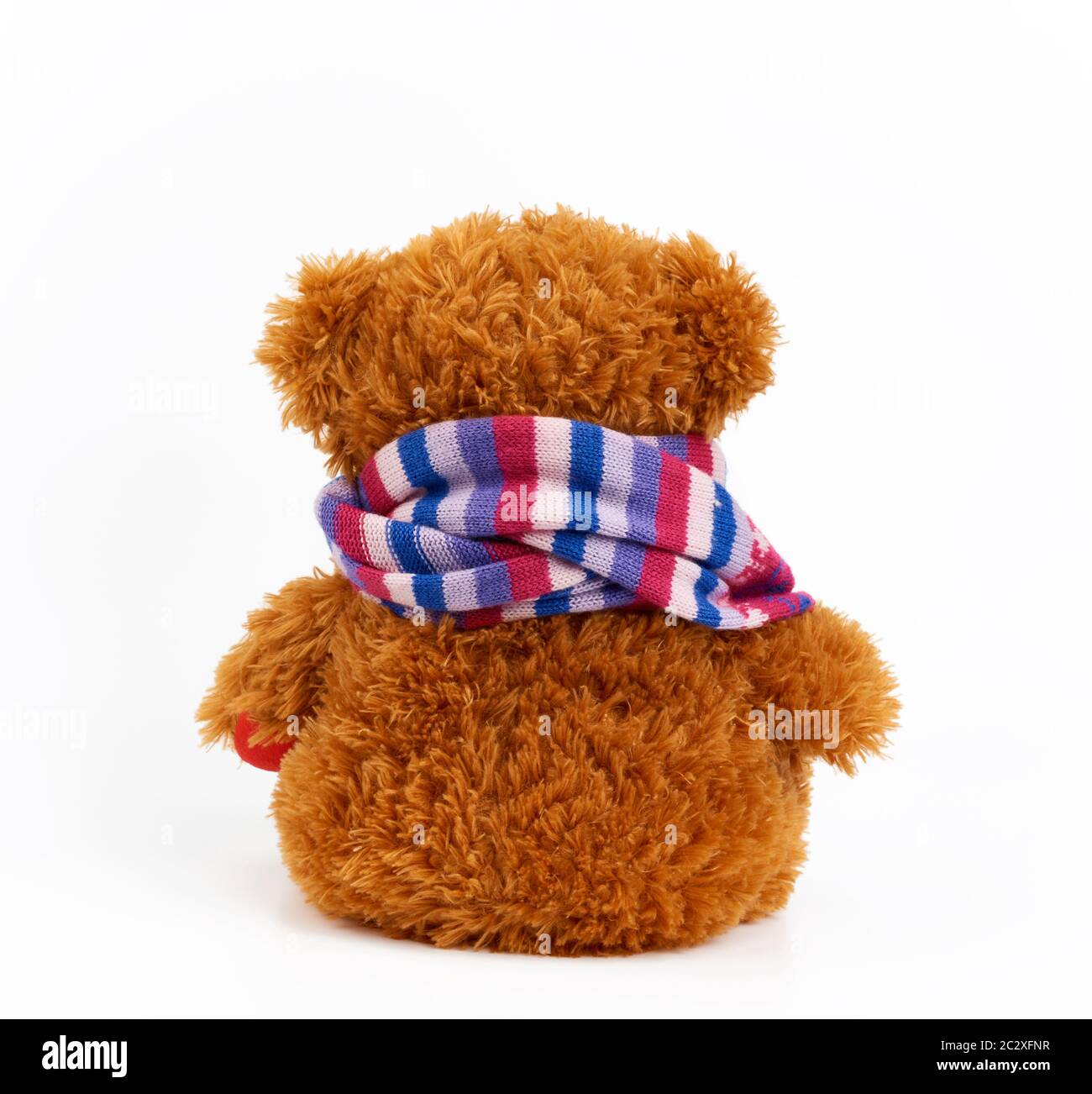 l'orsacchiotto di colore curly marrone siede con la sua parte posteriore su uno sfondo bianco, sciarpa multi-colorata di maglia è legata intorno al collo di un giocattolo dei bambini Foto Stock