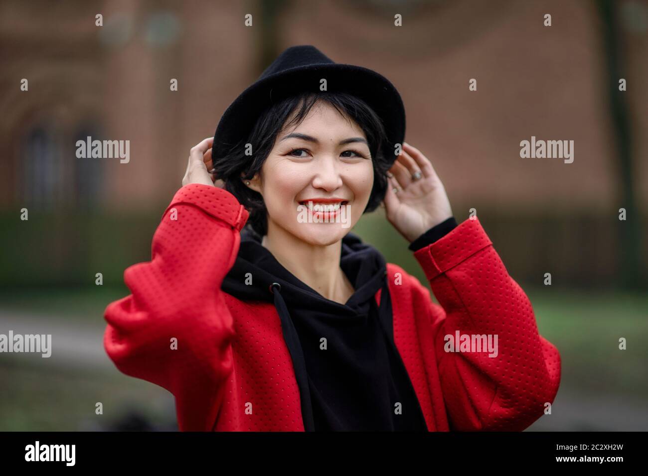 Ragazza orientale in un cappotto rosso elegante e cappello nero in un ambiente urbano Foto Stock