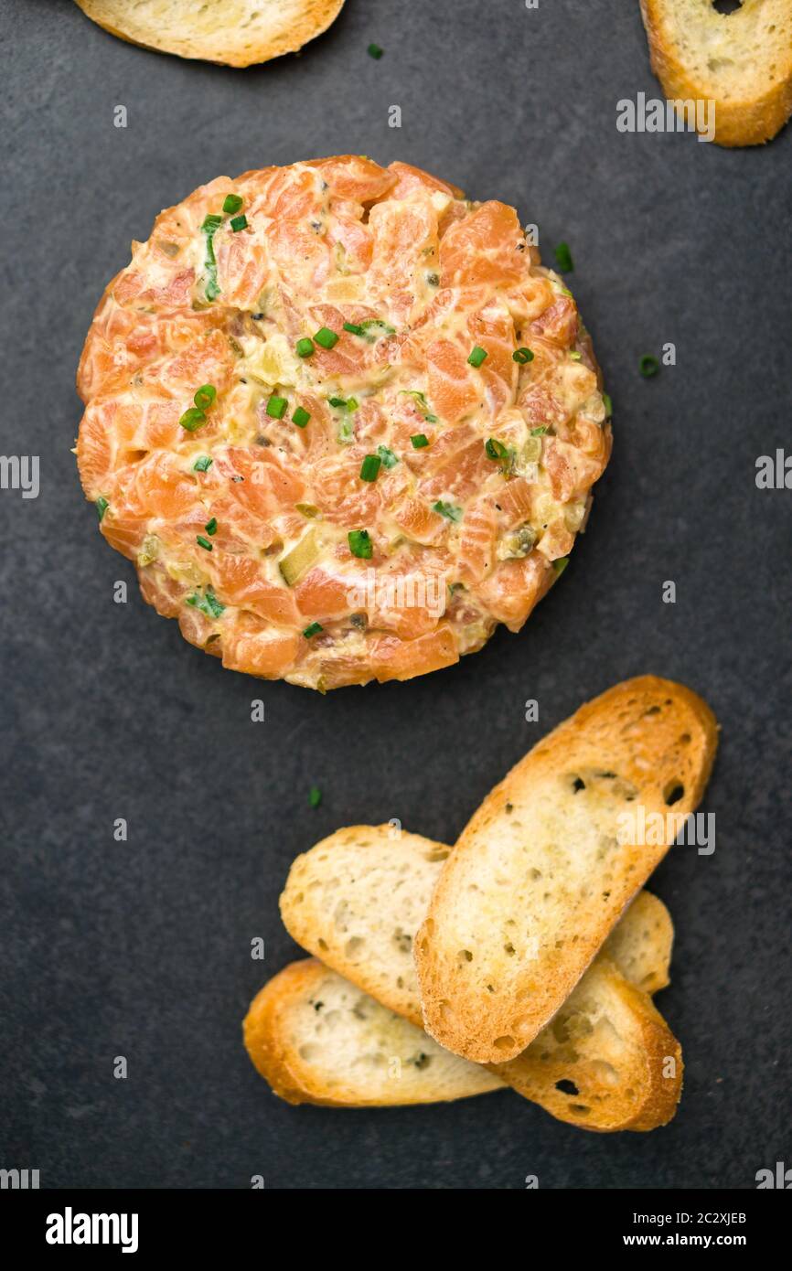 La tartare di salmone è preparata con pesce fresco fresco e crudo di salmone, avocado, salsa tartaro e cracker o pane. Questo piatto sano è spesso servito come antipasto Foto Stock