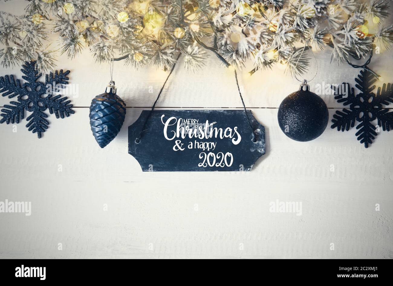 Natale nero piastra con testo in inglese Buon Natale e Felice 2020. Ramo di abete con le luci fairy su sfondo di legno Foto Stock