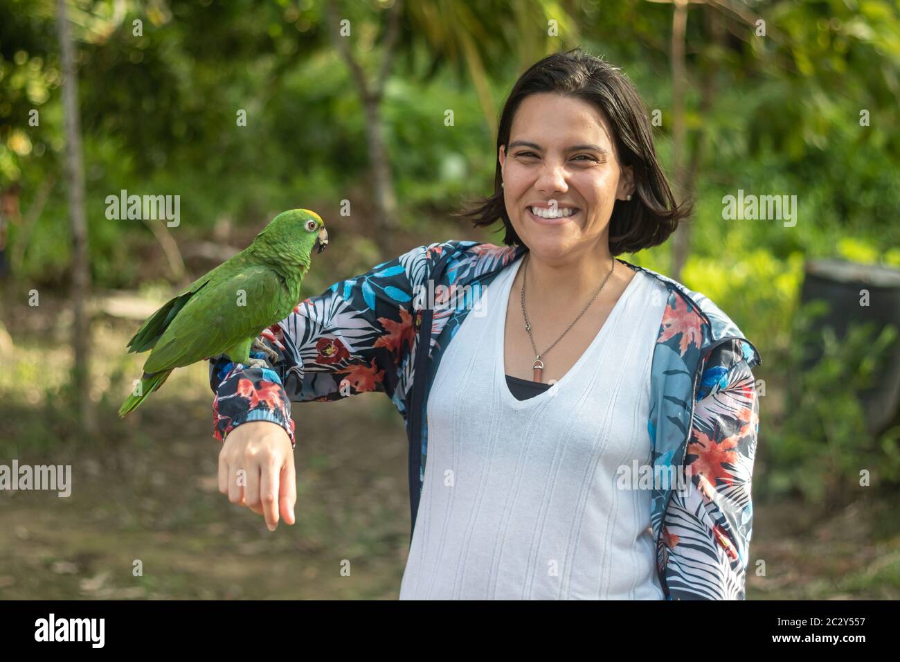 La donna si pone con un sorriso mentre porta il braccio ad un macaw in un accampamento Foto Stock