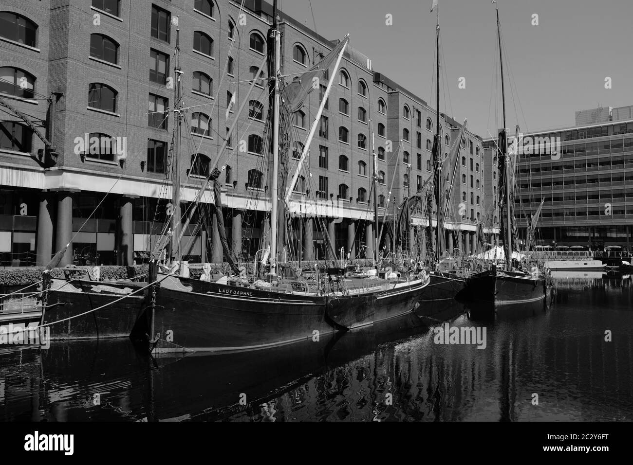 Tradizionali chiatte a vela nel molo di St. Katherine, Londra UK, con sfondo di magazzini originali convertiti. Immagine in bianco e nero. Foto Stock