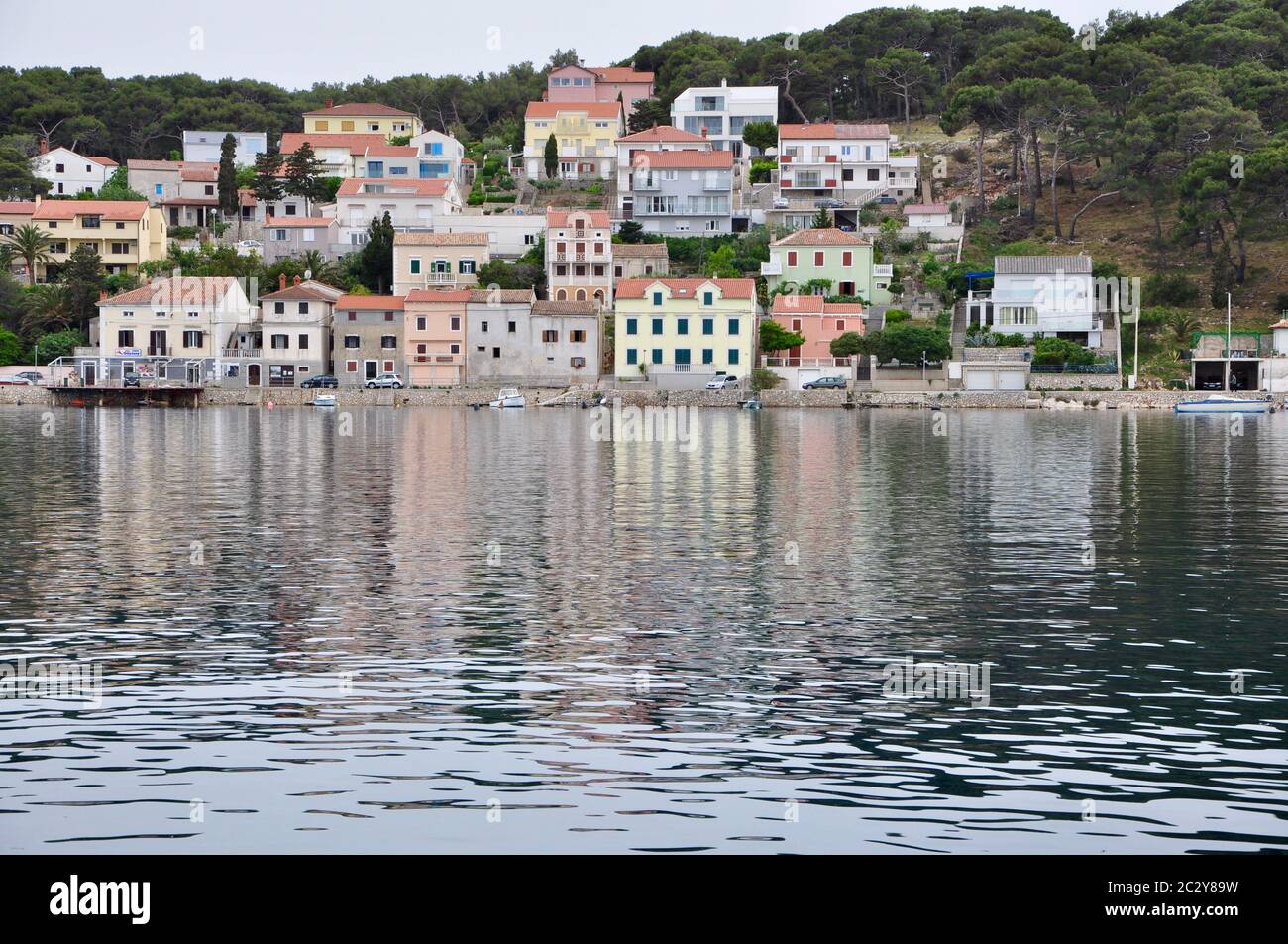 Paesaggio urbano sulla luce del giorno a riflessione nella laguna dell'isola di Lussino, lungomare e porto. Città mediterranea Mali Losinj sulla costa del mare Adriatico Foto Stock