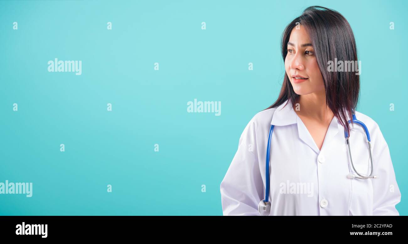 Ritratto asiatico bella donna medico sorridente suo stare con Le Mani in tasche su sfondo blu, con spazio copia per il testo Foto Stock