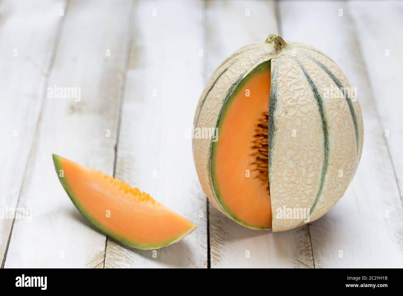 Taglio di melone al miele aperto su sfondo bianco di legno. Foto Stock