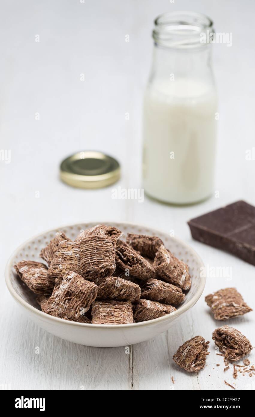 Fiocchi di grano al cioccolato in un recipiente e una bottiglia di latte. Foto Stock