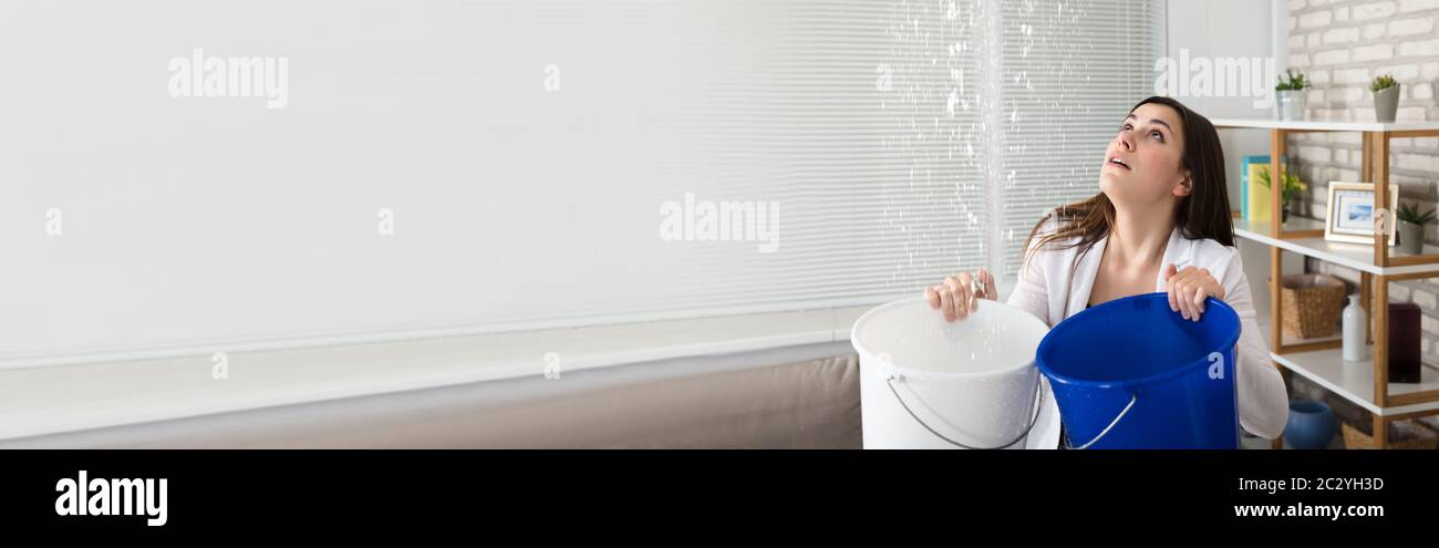 Young Female Preoccupato Woman Holding Benna Mentre Gocce D'Acqua Che Perdono Dal Soffitto Foto Stock