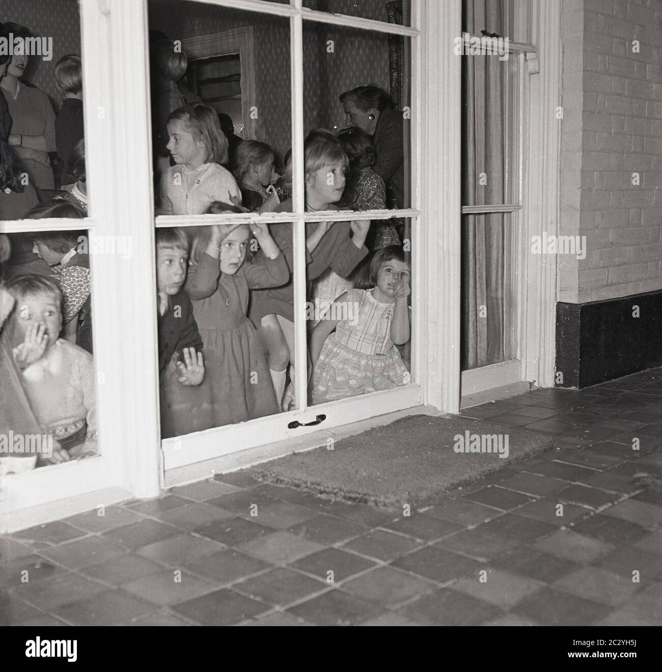 Anni '60, storico, un grouo di bambini eccitati a una festa in una casa che  si sbirciano le finestre sul retro della casa al patio esterno per provare  a vedere la sorpresa,