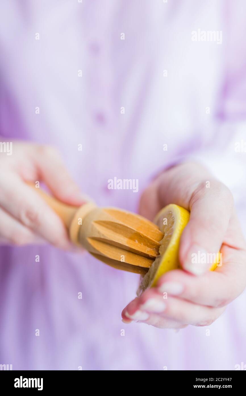 Mani femminili spremono il succo di limone fresco con alesatore in legno, concetto limonata. Foto Stock