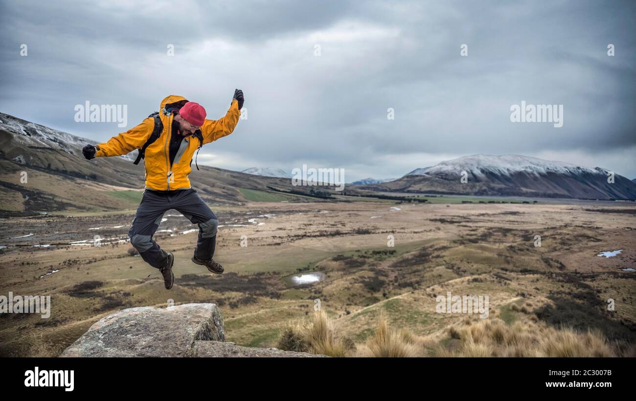 Escursionista maschio, fa un salto gioioso, Rangitata River Valley, Ashburton Lakes, Ashburton, Canterbury, Nuova Zelanda Foto Stock