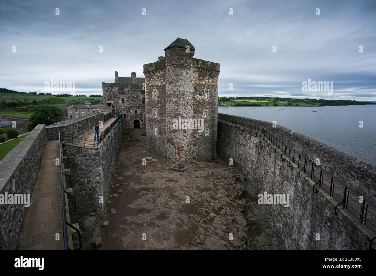 Un turista maschile si erge sul balcone che si affaccia sul castello di Blackness, a forma di nave, mentre si visitano i siti cinematografici del popolare viaggio nel tempo Outlander Foto Stock