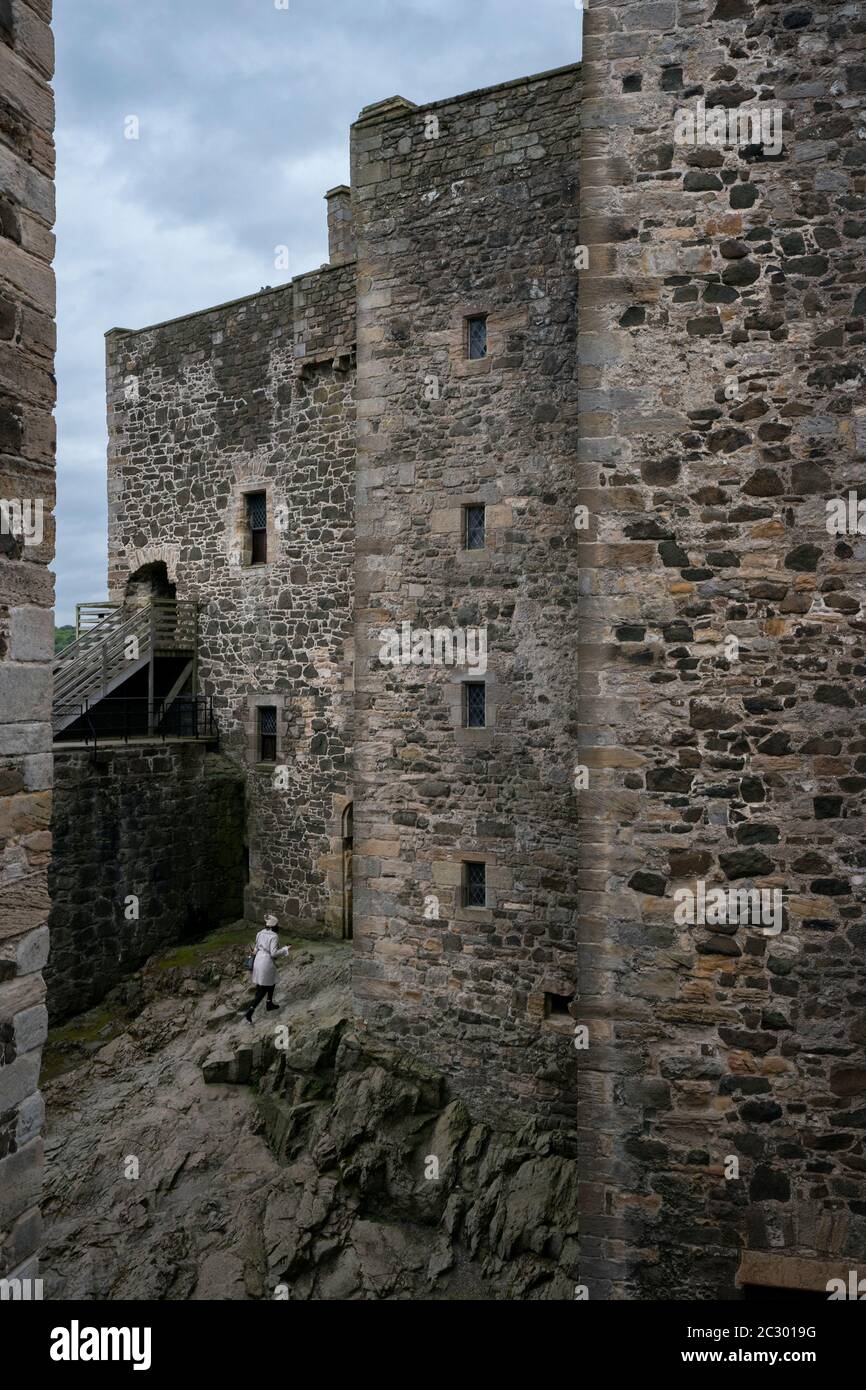 Una donna turistica passeggiate attraverso la base rocciosa del castello di Blackness a forma di nave, mentre visita i siti di film del popolare viaggio tempo Outlander tv Foto Stock