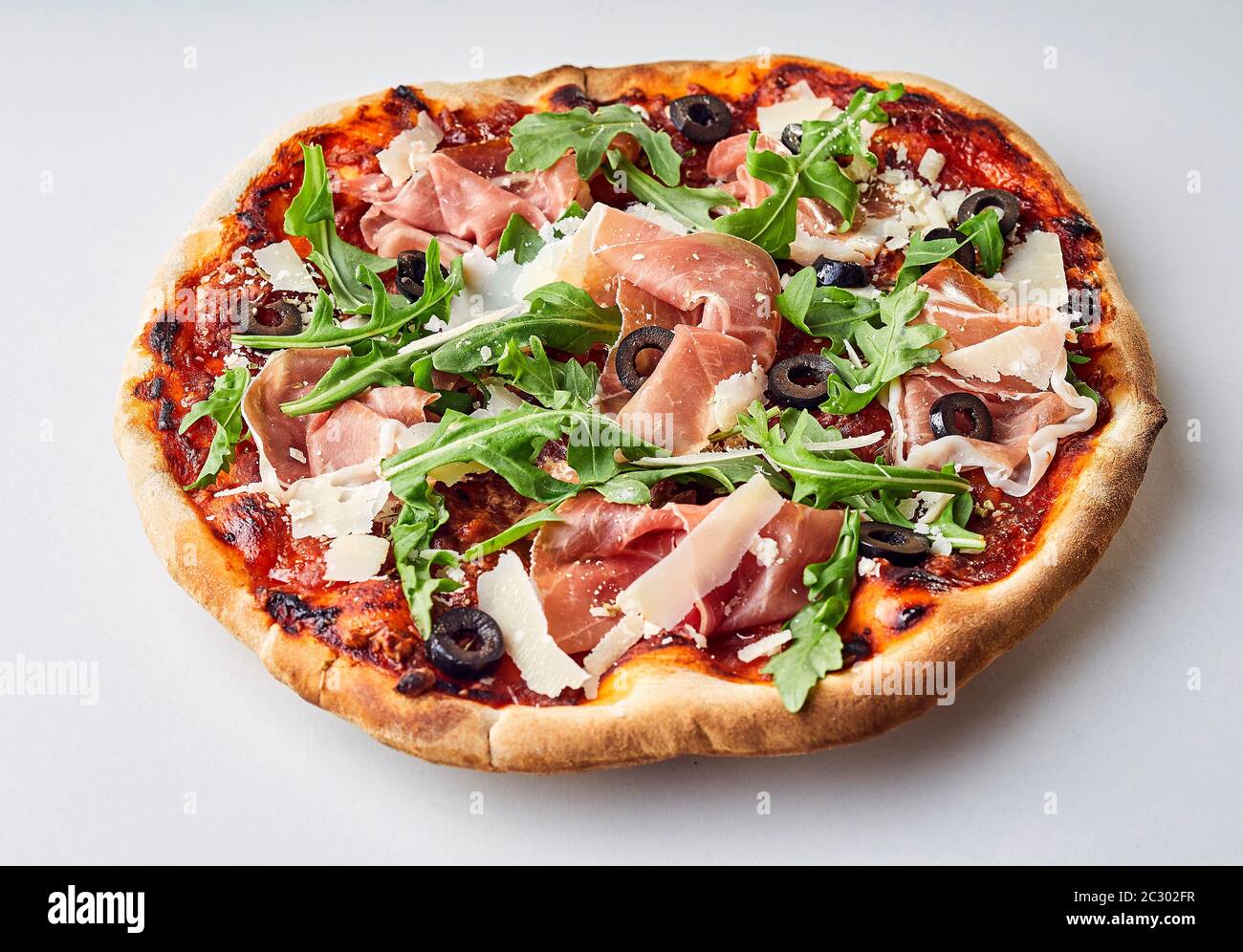 Prosciutto gourmet e rucola pizza italiana condita con parmigiano e olive in scaglie su sfondo bianco in primo piano per la pubblicità dei menu Foto Stock