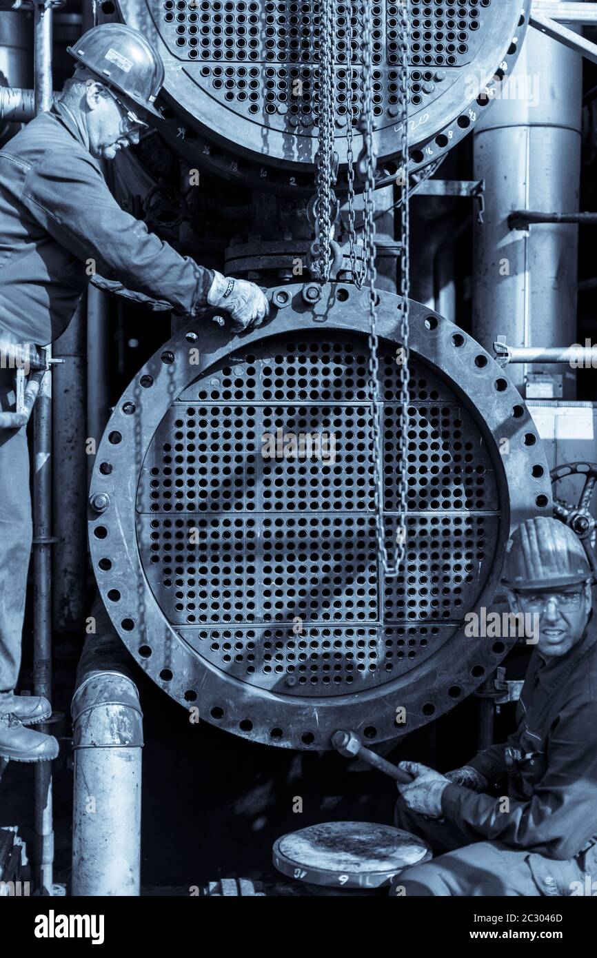 Due lavoratori stanno assemblando uno scambiatore di calore in un impianto chimico. La lastra di tubo è visibile quando il canale è stato rimosso. Foto monocromatica. Foto Stock