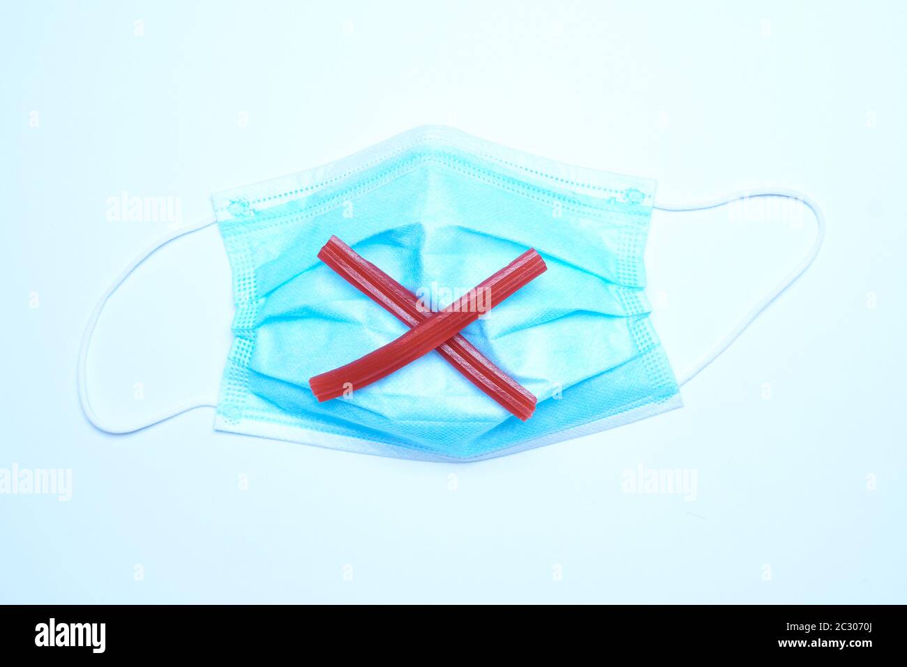 Icona rossa con la x contrassegnata con la liquirizia sopra una maschera medica. Foto Stock