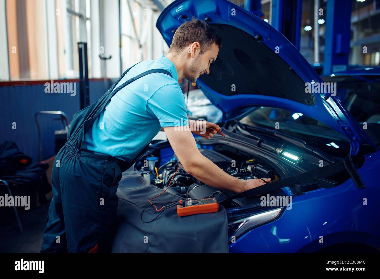 L'elettricista automatico in uniforme controlla i circuiti elettrici sulla stazione di servizio dell'automobile. Controllo e ispezione di automobili, diagnostica professionale e riparazione Foto Stock