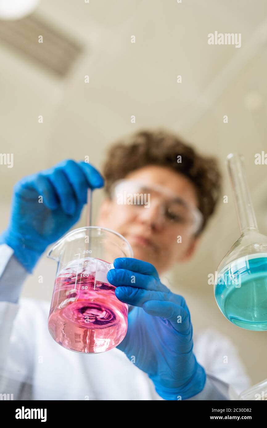 Vista dal basso del chimico nei guanti protettivi che agita i reagenti nel bicchiere durante la preparazione per l'esperimento Foto Stock