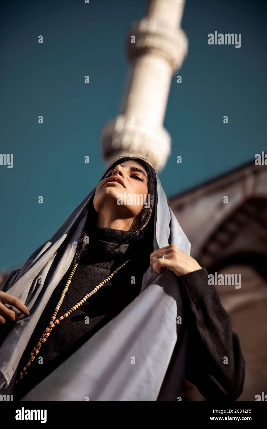 Ritratto di uno splendido modello arabo posto vicino alla moschea, indossando sciarpa tradizionale islamica, abito in stile musulmano, splendida donna attraente, arabo Foto Stock