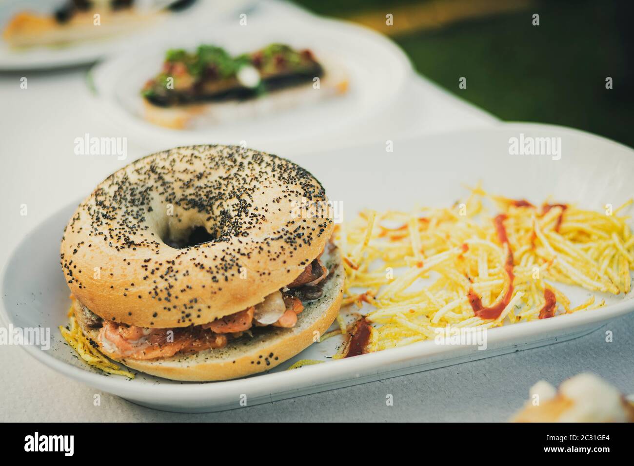 Piatto proposto in una festa gastronomica composta da un bagel con semi e farcito con frutti di mare con patatine di paglia Foto Stock