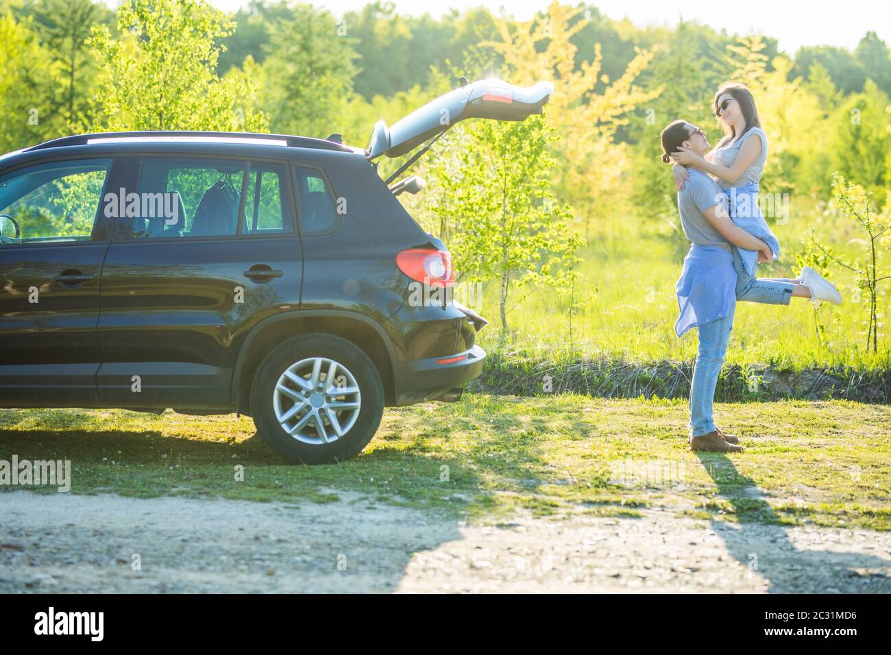 Bell'uomo che carrava la sua ragazza sorridente sul retro vicino all'auto al tramonto Foto Stock