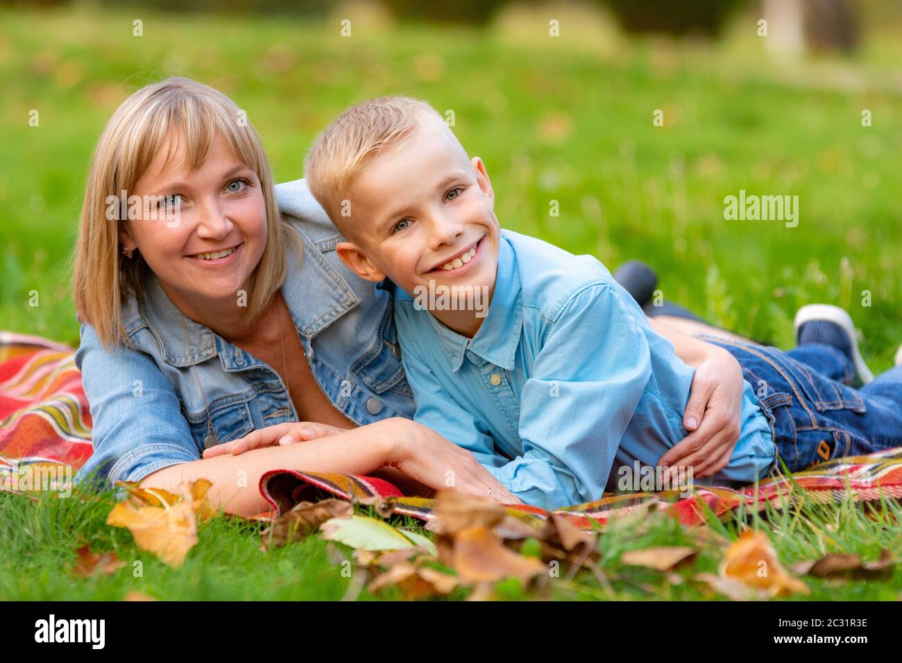Mamma giovane e figlio adolescente si trovano sul copriletto in erba nel parco della città Foto Stock