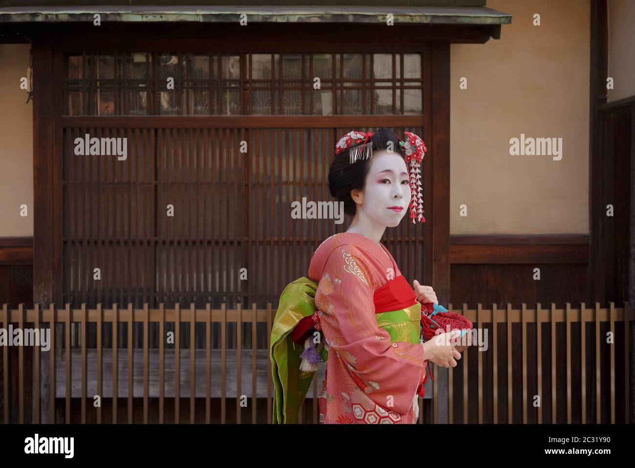 Maiko in un kimono a piedi nella parte anteriore della porta di una casa tradizionale giapponese di Kyoto. Foto Stock