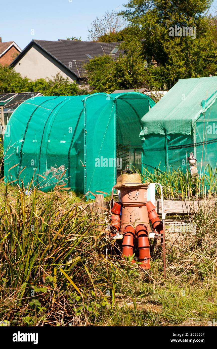 Plantpot uomo su un sito di assegnazione seduta su una sedia da erba lunga. Tutta la figura è fatta da pentole di pianta di dimensioni differenti Foto Stock