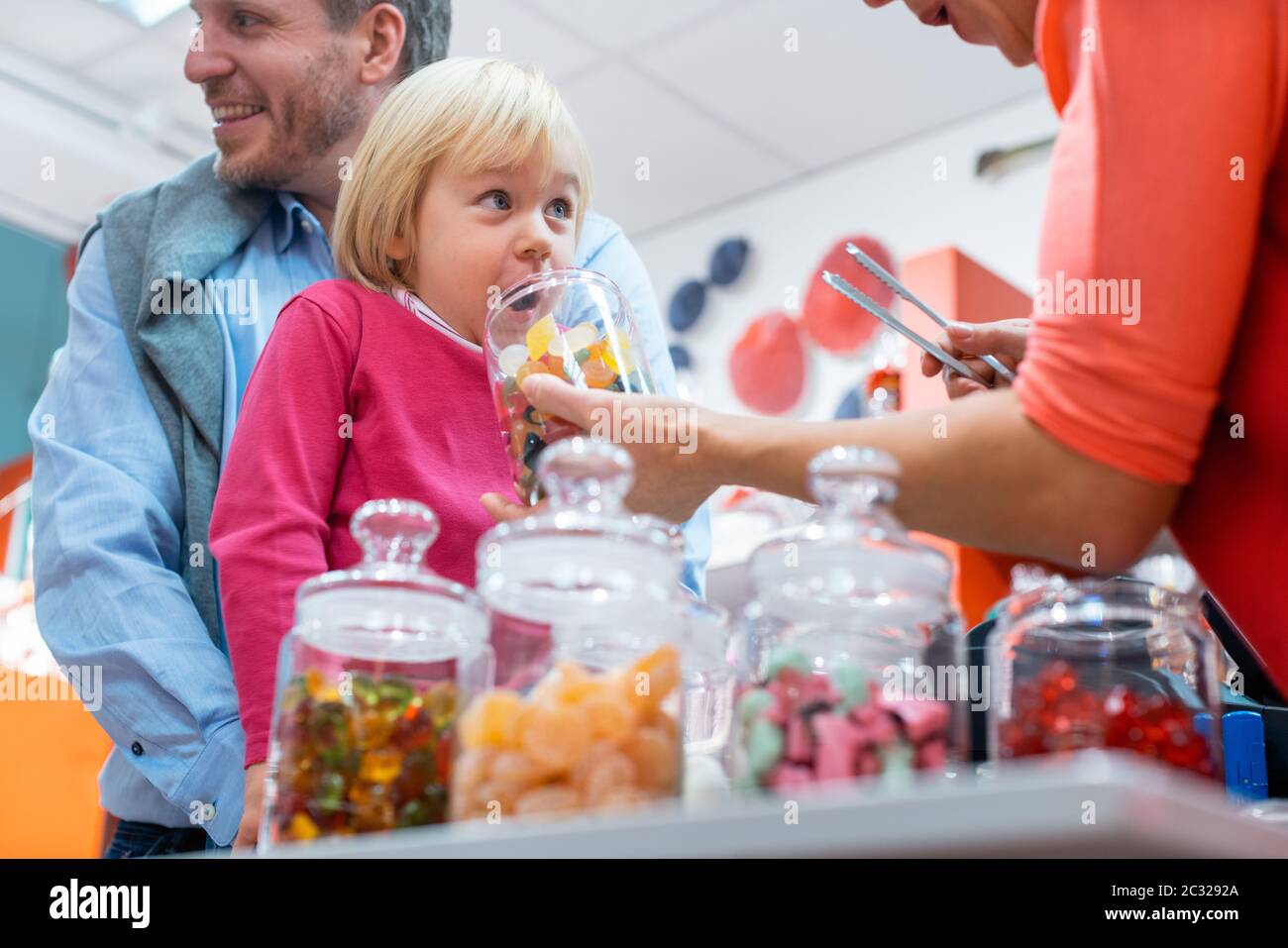 Saleslady per le cose dolci che porgono una caramella ad un capretto che è tenuto dal suo padre Foto Stock