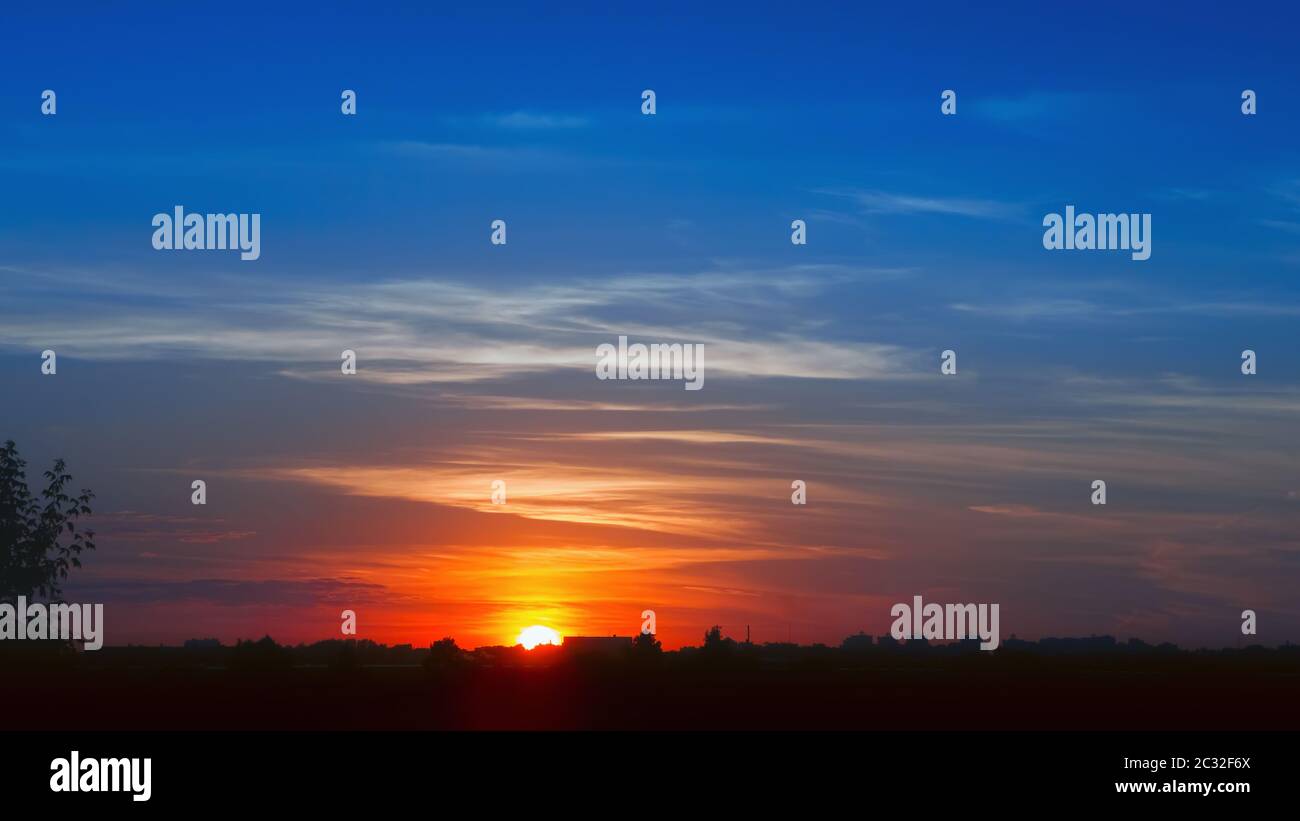 Colori fieri del sole che tramonta nel cielo serale sulle sagome della città. Sfondo pittoresco tramonto con spazio per la copia. Filtro sfocato Foto Stock