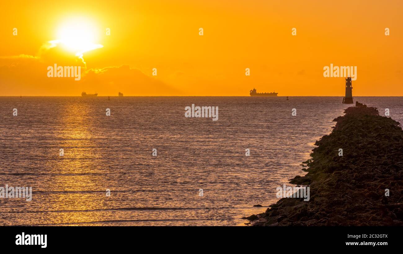 Silhouette di navi da carico. Disco solare, splende da dietro la nuvola. Faro su Bull Island Foto Stock