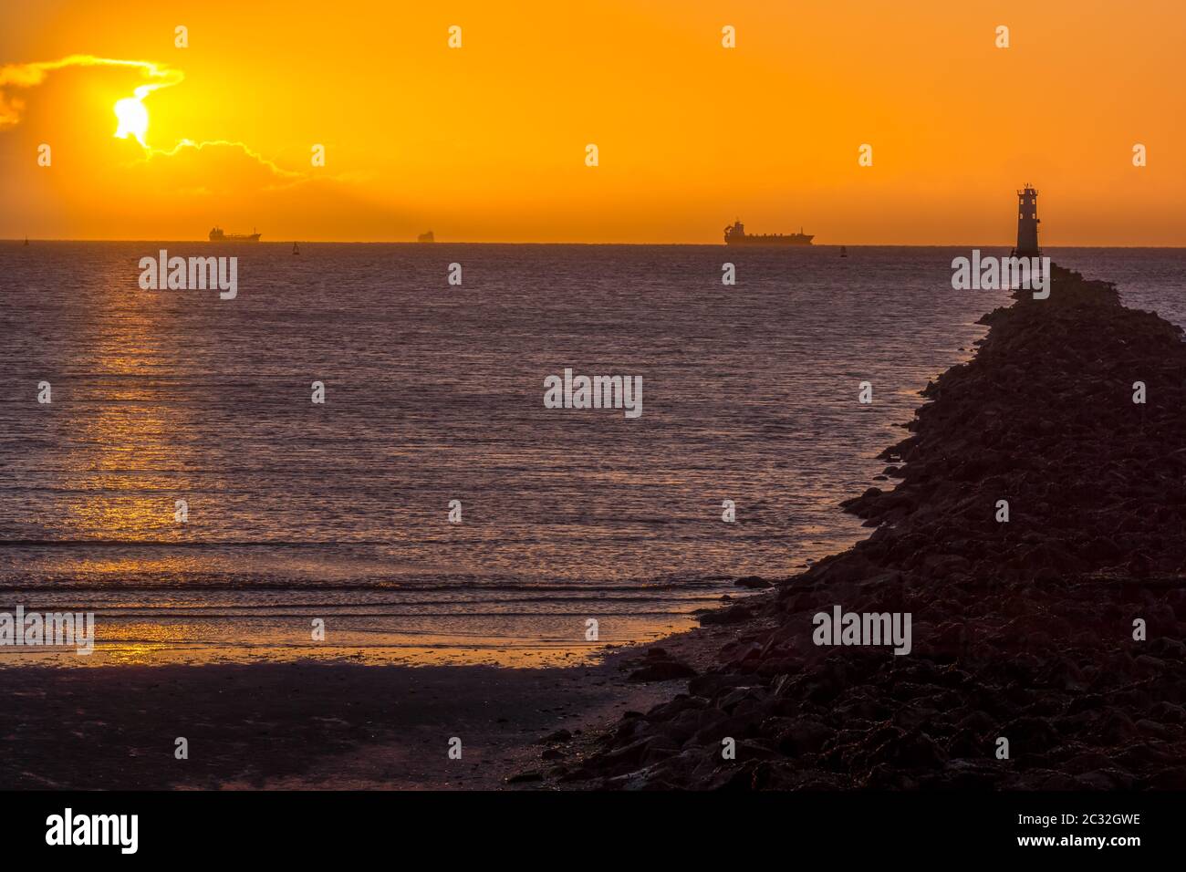 Silhouette di navi da carico. Disco solare, splende da dietro la nuvola. Faro su Bull Island Foto Stock