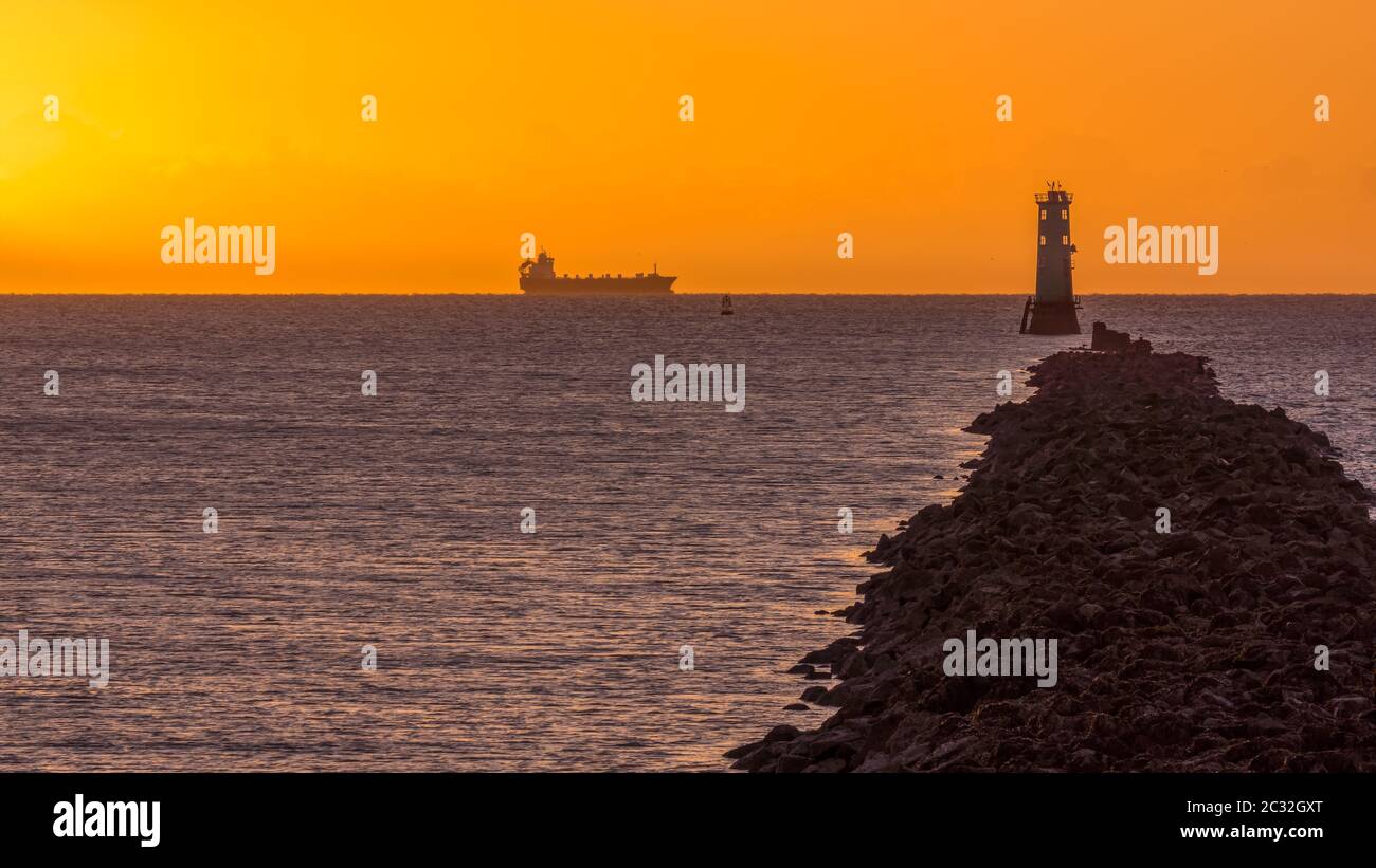 Silhouette di nave da carico all'ora d'oro con faro su Bull Island Foto Stock