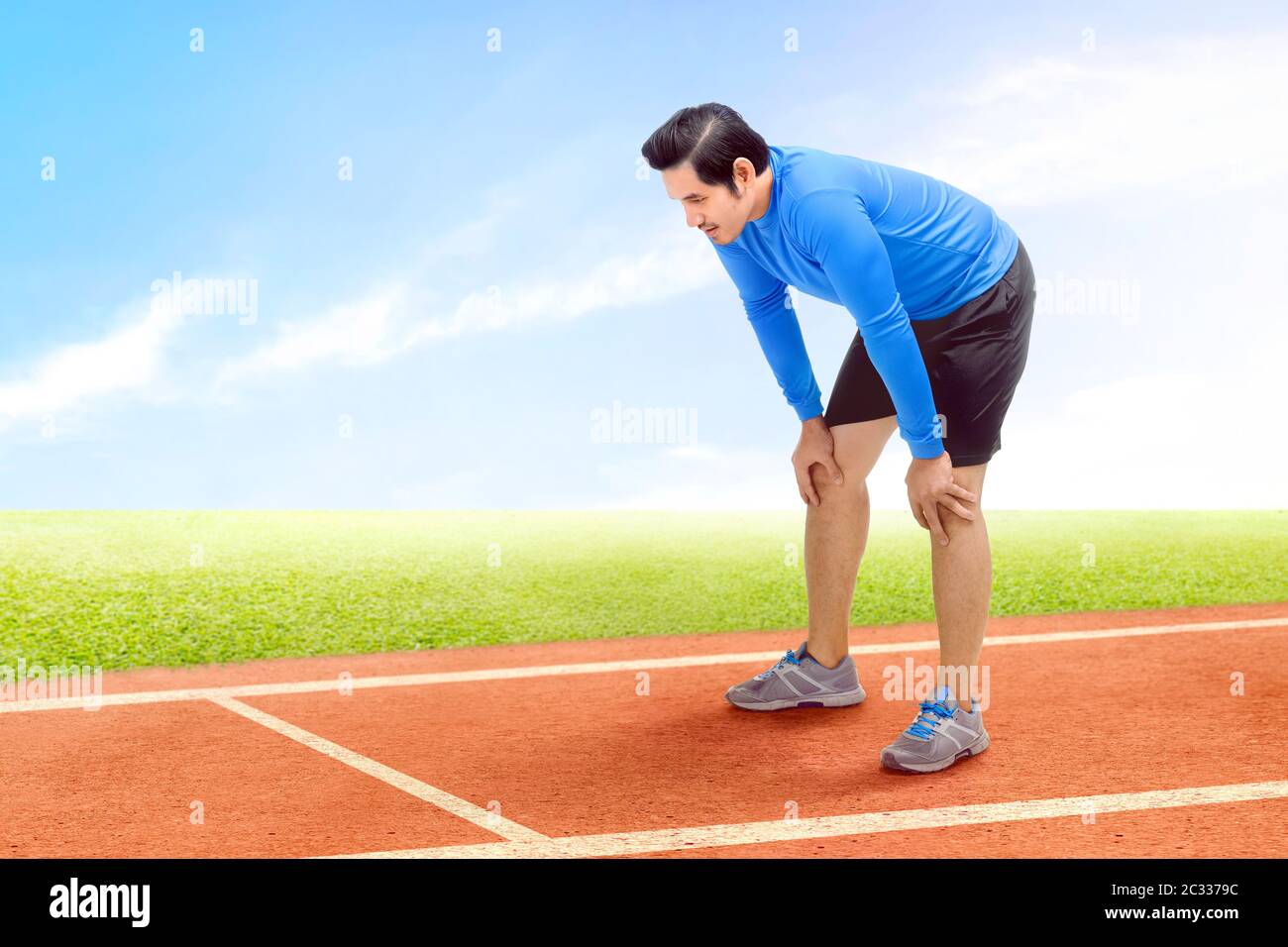 Asian runner uomo prendere una pausa dopo aver eseguito sulla via di corsa con un cielo blu sullo sfondo Foto Stock