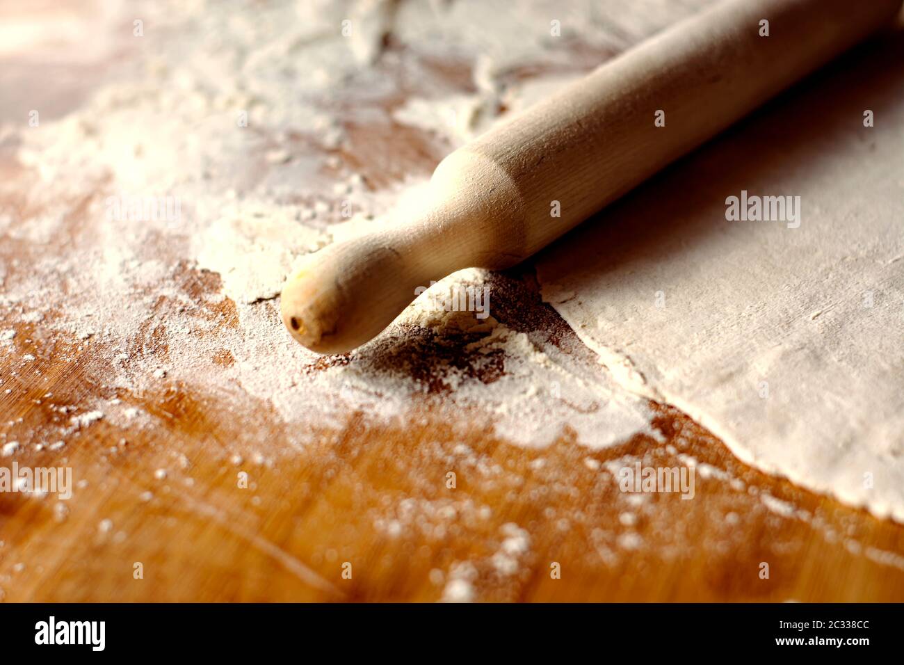 un mattarello sopra l'impasto su un pannello di legno sporco di farina. Preparazione di alimenti a base di farina prima di essere cotti Foto Stock