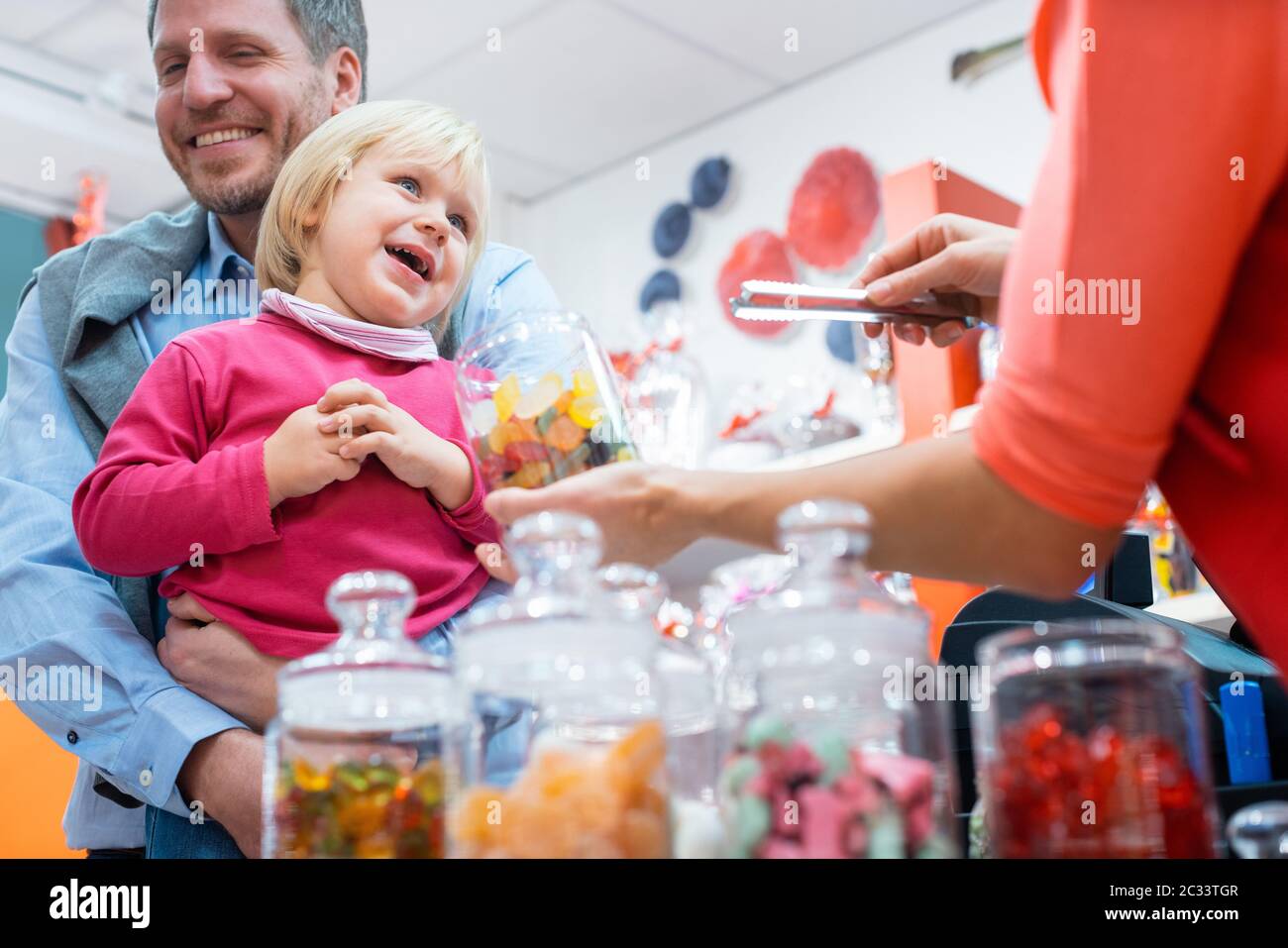 Saleslady per le cose dolci che porgono una caramella ad un capretto che è tenuto dal suo padre Foto Stock