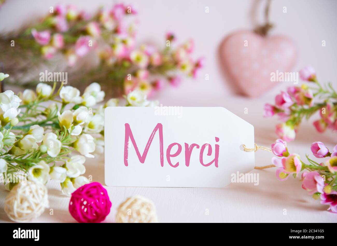 Etichetta con testo francese merci significa grazie. Rosa e fiori bianchi con decorazione del cuore. Foto Stock
