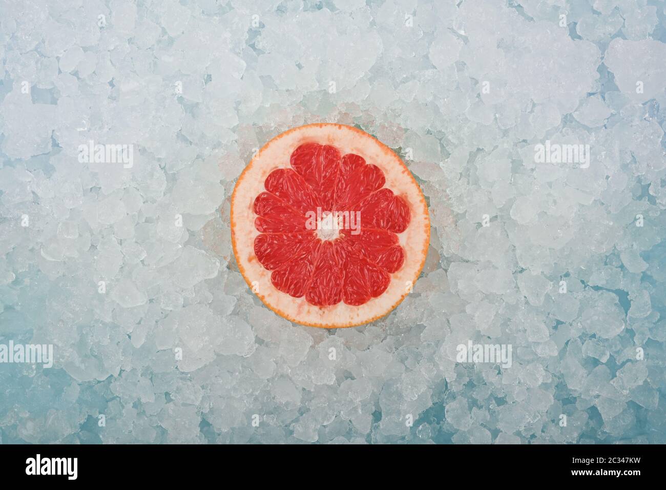 Primo piano una fetta di pompelmo rosa appena fresca sullo sfondo del ghiaccio tritato, vista ad alta angolazione, direttamente sopra Foto Stock