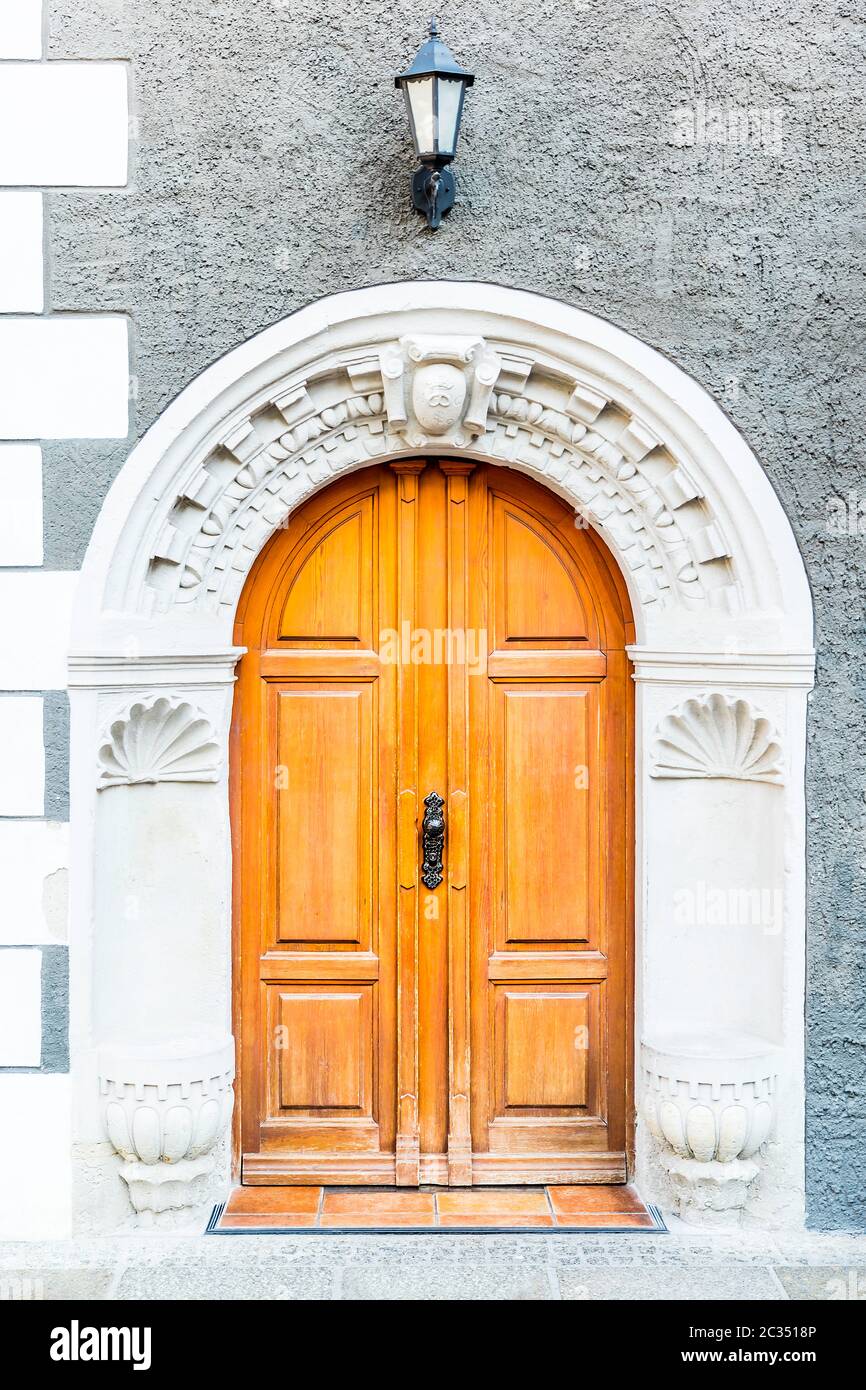 Portale d'ingresso storico del 1660 con stemma in arco rotondo. Arco riccamente decorato con ornamenti con una porta di legno gialla a doppia foglia. Foto Stock