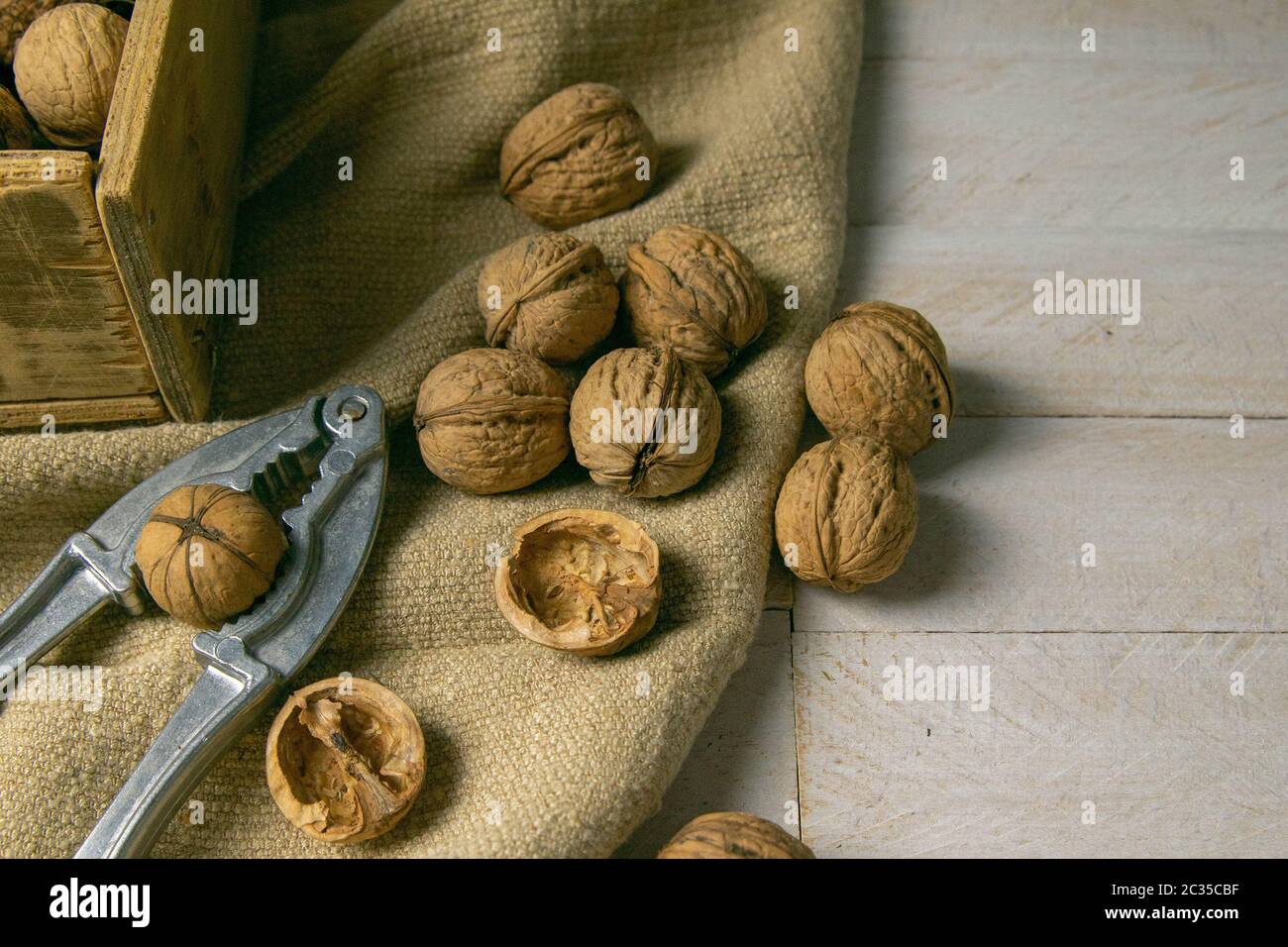 Noci in una scatola di legno, che si trova su un vecchio sacco rustico, anche sparso su un tavolo bianco nelle vicinanze è un cracker di noce. Foto Stock