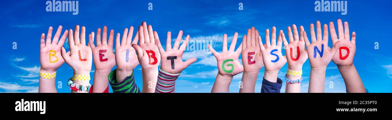 Kids Hands Holding colorato tedesco parola Bleibt Gesund significa rimanere in salute. Cielo blu come sfondo Foto Stock