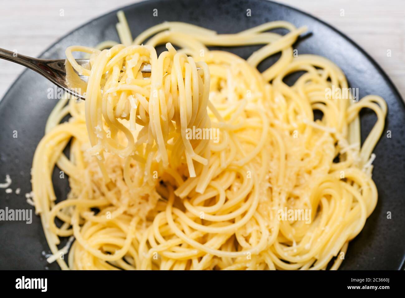 Vista superiore della forcella con spaghetti al burro e parmigiano (pasta con burro e formaggio) chiudere fino oltre la piastra nera su grigio tavolo in legno Foto Stock