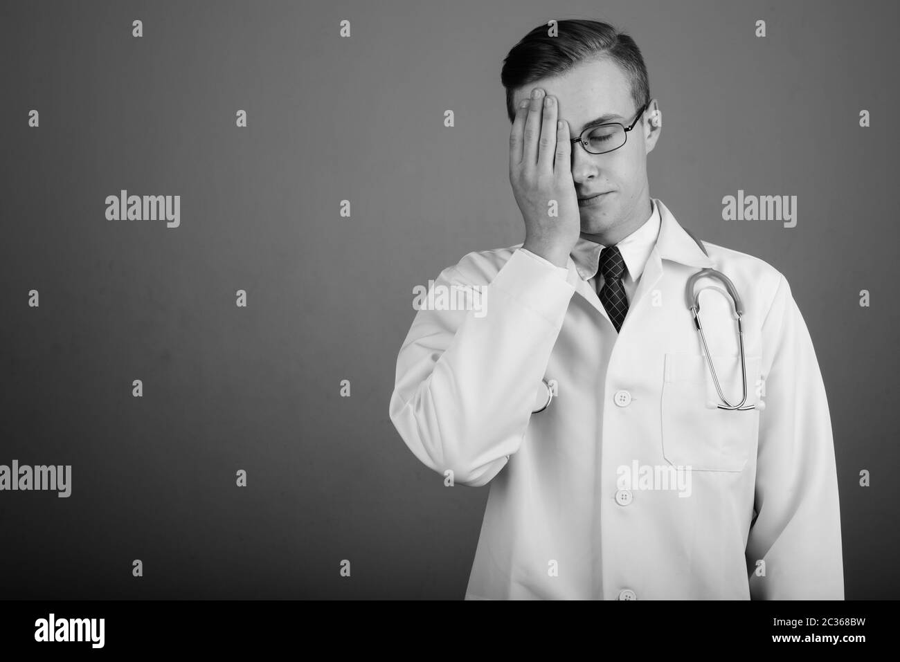 Giovane uomo bello medico contro uno sfondo grigio Foto Stock