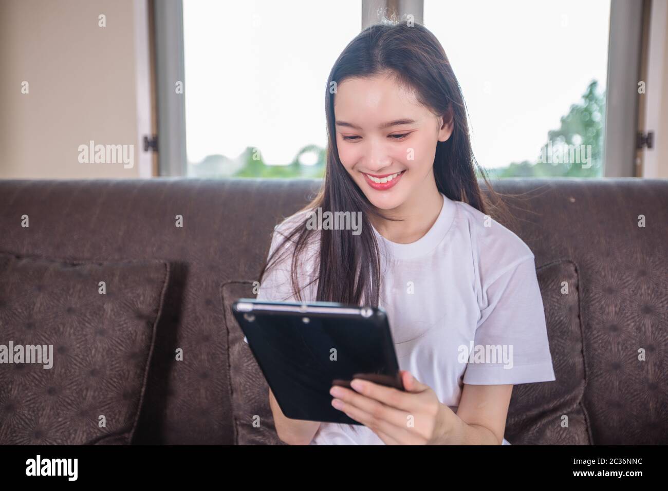 Asian giovane donna felice allegro cute bello è giocare a computer tablet pad digitale e sedersi sul divano a casa, sorridente signora utilizzando app reading Foto Stock